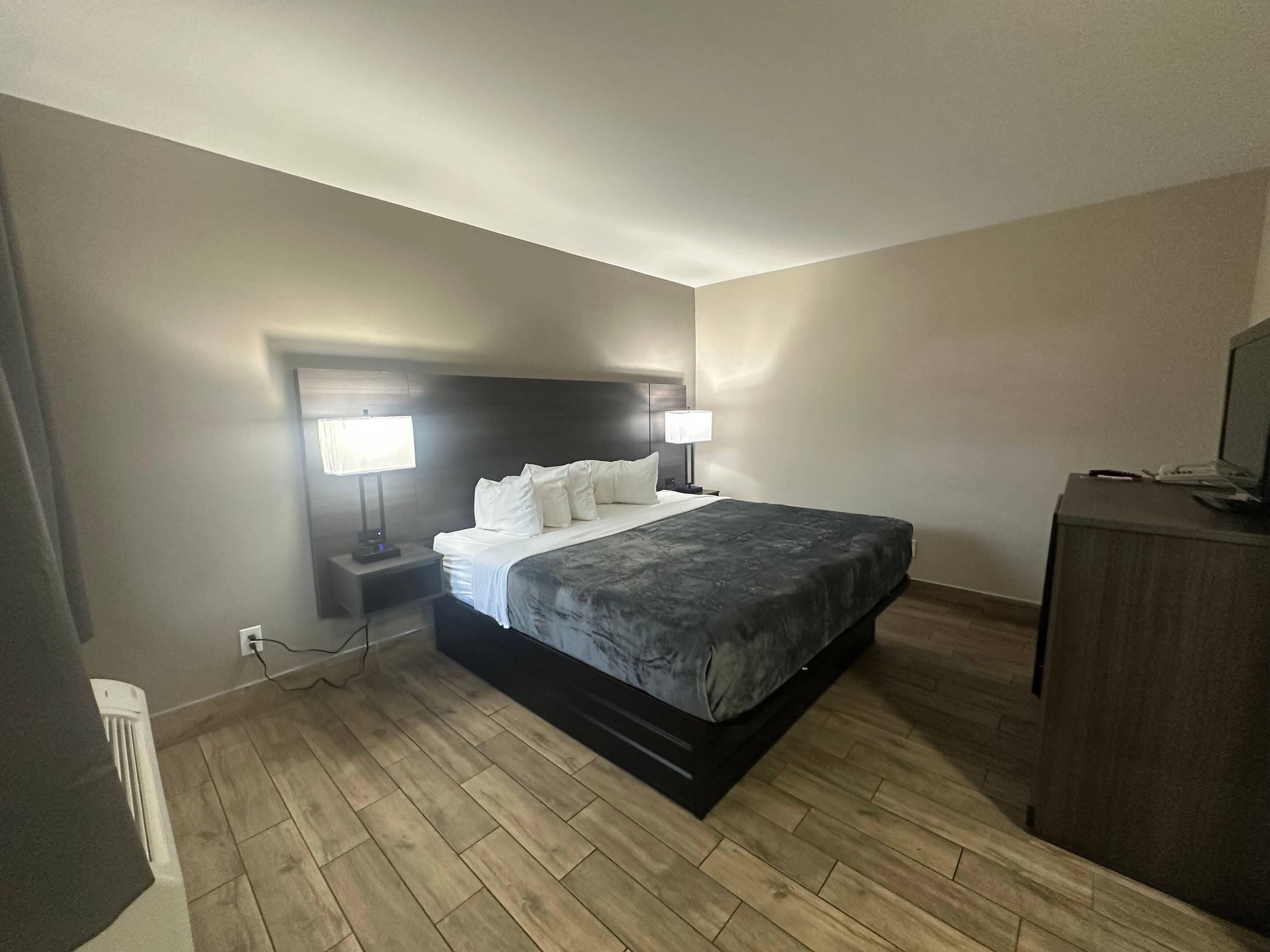 Une chambre d’hôtel avec un lit, deux lampes de chevet, un bureau avec un ordinateur et une commode.