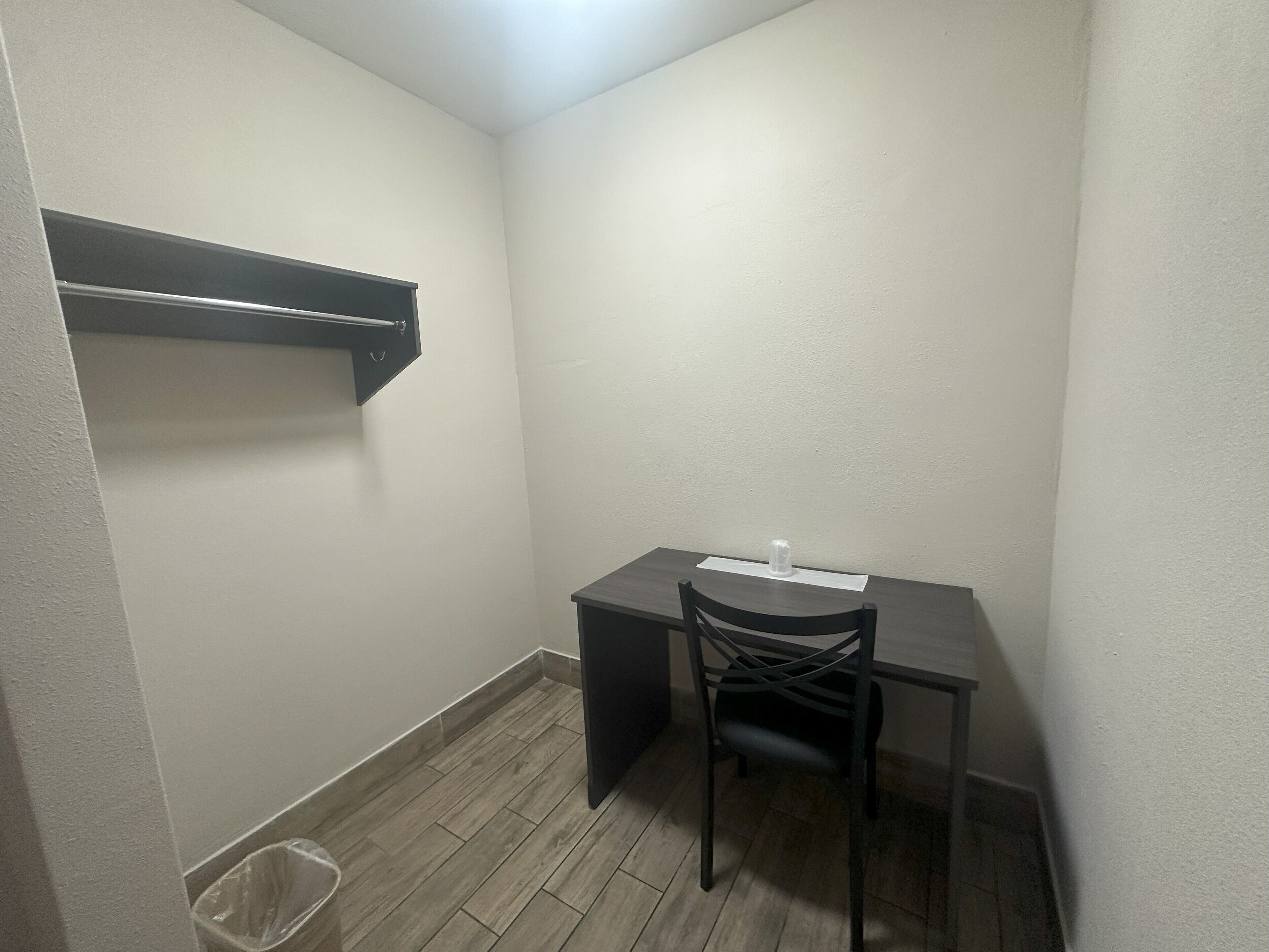 A small, dimly lit room with a desk, chair, and a trash bin.