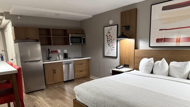 A compact hotel room with a kitchenette, a bed with white bedding, a red chair, and a wooden headboard. - Hotel Kiva, An Ascend Collection Hotel (Albuquerque)