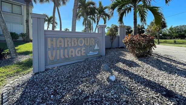 Señal de Harbour Village con un gráfico de un velero, rodeado de palmeras y un camino de grava.