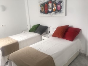 Two single beds with white bedding, a green and a red pillow, and a wall-mounted artwork above them. - Seaside 2 Bedroom Condo Fuengirola Spain (Fuengirola)
