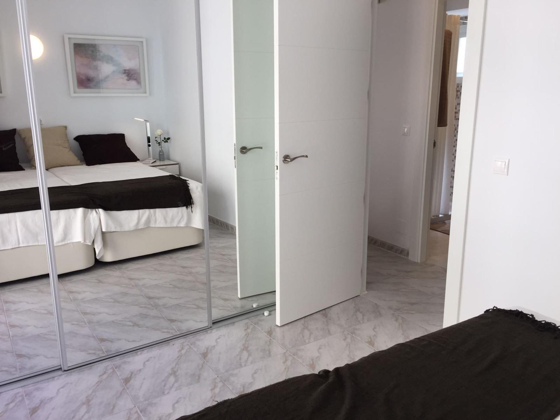 Een slaapkamer met een bed, nachtkastje, spiegel en deur.