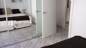 A bedroom with a bed, a bedside table, a mirror, and a door. - Seaside 2 Bedroom Condo Fuengirola Spain (Fuengirola)