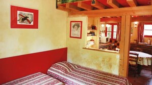Een kamer met twee bedden, een kleurenpalet van rood en wit, een houten plafond en uitzicht op de keuken.