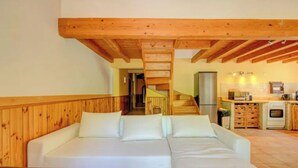 A cozy room with a wooden ceiling, a white sofa, a small table, and a kitchen area with cabinets and appliances. - Cézanne - Comfort, space and relaxation for families and friends, park view (ARLES)