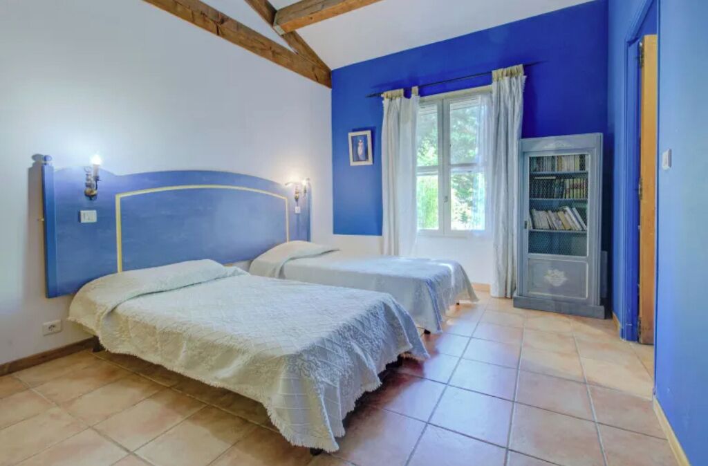 Une chambre avec deux lits, une bibliothèque et une fenêtre avec des rideaux.