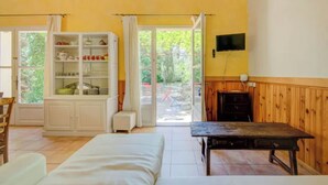 A room with a bed, a table, a cabinet with dishes, a TV on the wall, and a view of the outside. - Cézanne - Comfort, space and relaxation for families and friends, park view (ARLES)