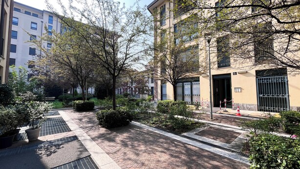 Une cour avec des allées pavées de briques, des plantes en pot et une entrée grillagée menant à un bâtiment.