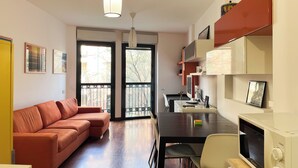 Un salon moderne avec un canapé, une table à manger et un téléviseur. Il y a un balcon avec vue sur les arbres.