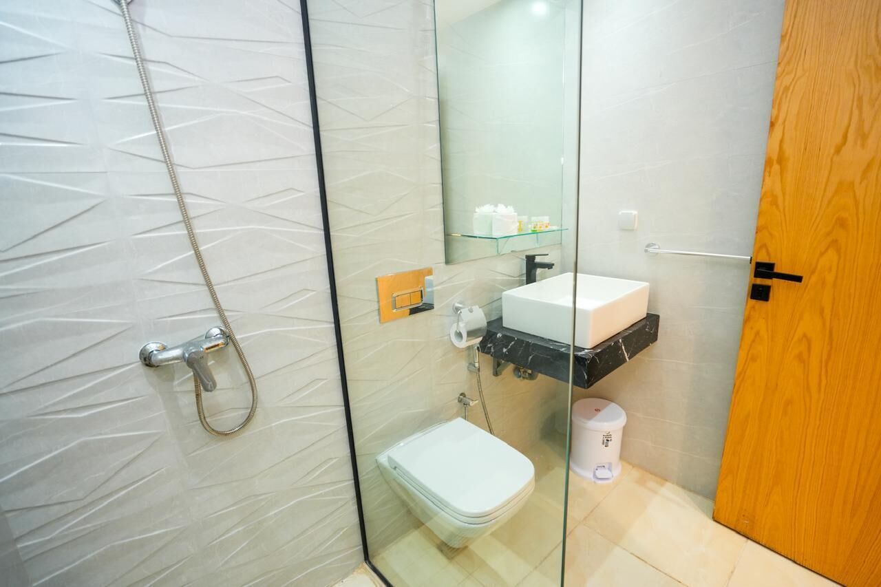 A modern bathroom with a glass shower enclosure, a white toilet, a sink with a black countertop, and a mirror above the sink.