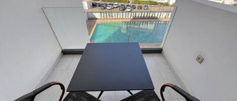 A balcony with a table and chairs, overlooking a swimming pool and residential buildings.