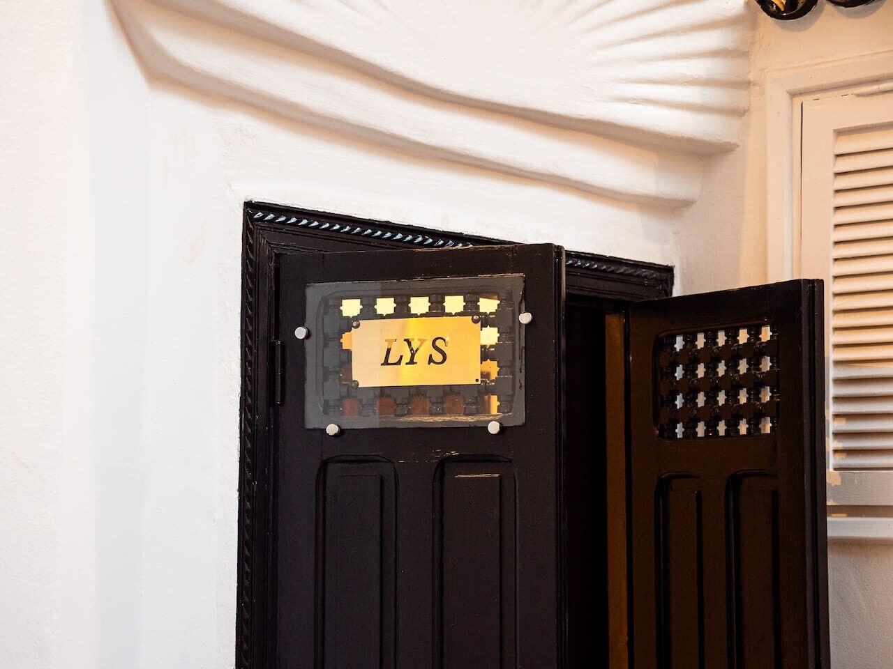 A black door with a nameplate reading "LYS" and a decorative panel.