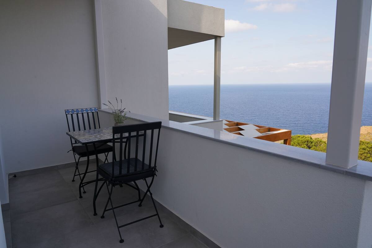 Een balkon met een tafel en stoelen, een bloempot en uitzicht op zee.