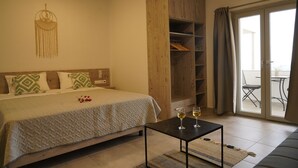 A bedroom with a bed, a wooden wardrobe, a small table with glasses, and a balcony with a chair. - House of Harmony Suites (Malevizi)