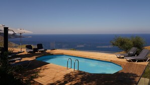 A wooden deck with a swimming pool, lounge chairs, and a view of the sea. - House of Harmony Suites (Malevizi)