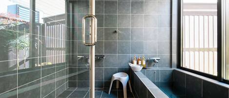 A modern bathroom with a glass shower enclosure, a white stool, and a vanity with toiletries.