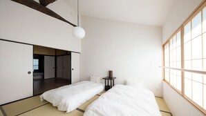 Une chambre de style japonais minimaliste, avec deux lits, des tatamis, une petite table et une grande fenêtre.