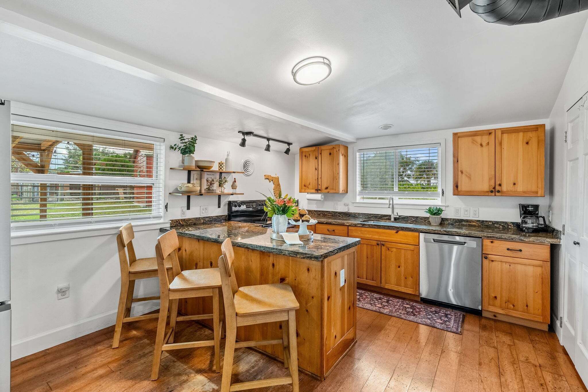 A kitchen with wooden cabinets, a granite countertop, a central island with bar stools, and a dishwasher.