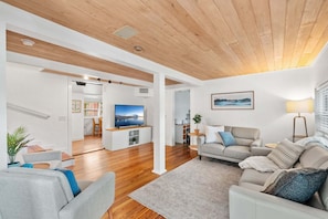 A modern living room with a wooden ceiling, a television, a sofa, a coffee table, and a dining area in the background. - 1061 Louisiana Avenue (Sebastian)
