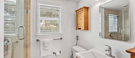 Une salle de bain avec une douche à parois de verre, des toilettes, un lavabo avec un miroir et un meuble en bois.