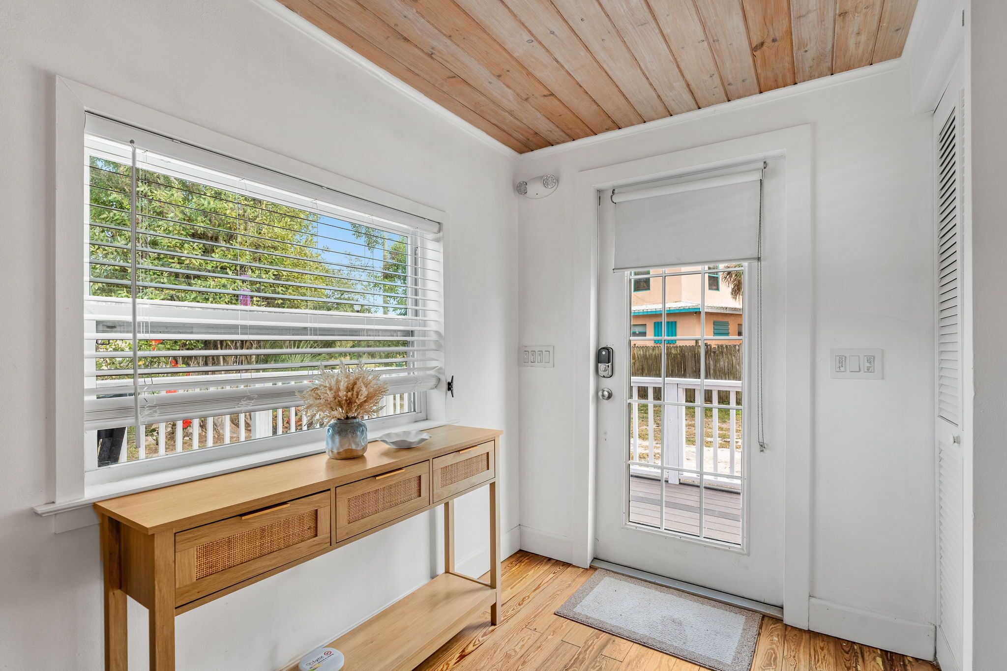Ein Zimmer mit Holzboden, einer weißen Tür mit Fenster und einem hölzernen Konsolentisch, mit Blick auf Grünflächen.
