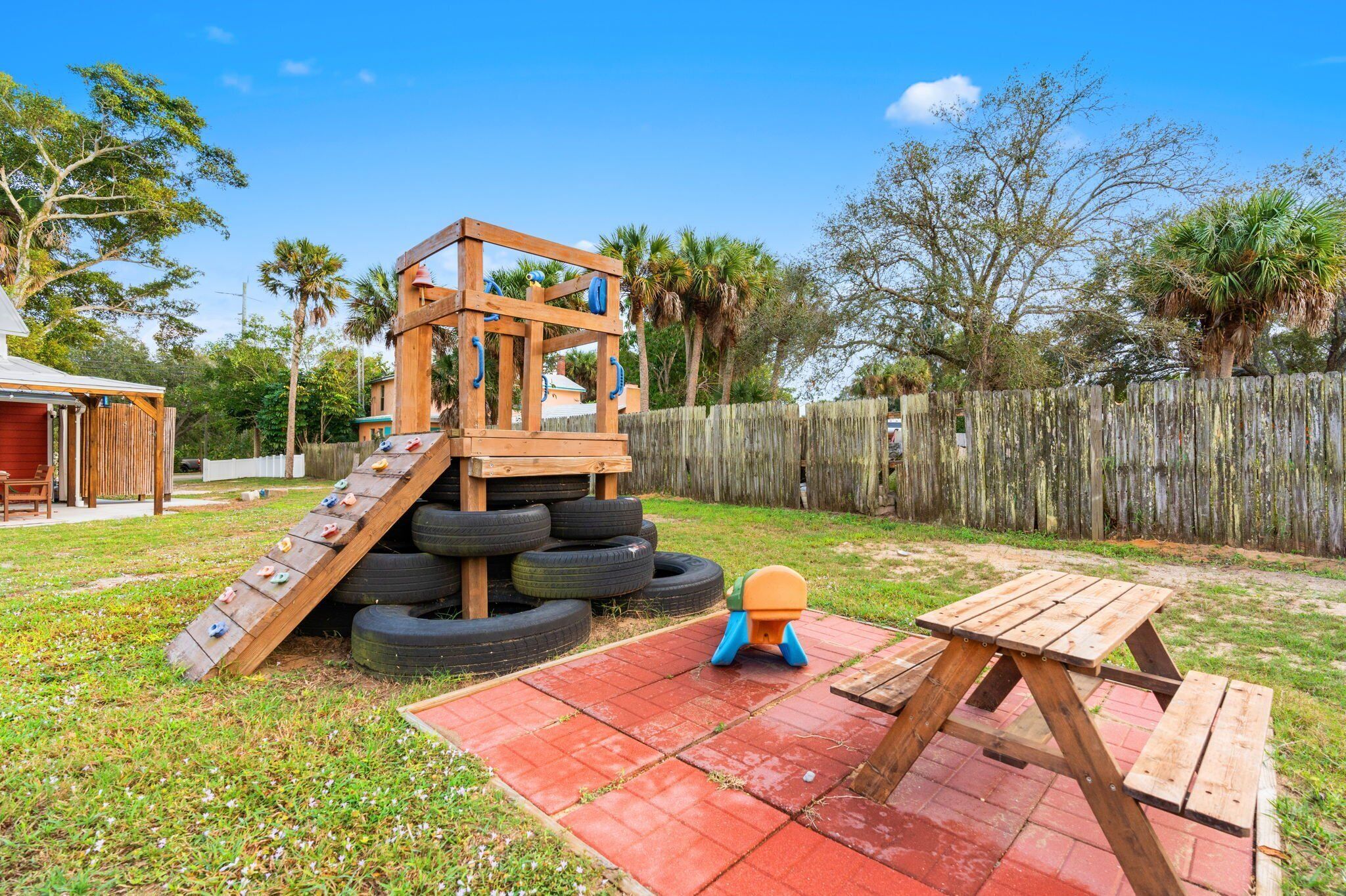 Una estructura de madera con tobogán y pared de escalada, una mesa de picnic y una rampa hecha con neumático.