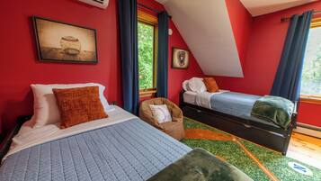 A room with two beds, a window with curtains, a framed picture on the wall, and a small chair with a baseball pillow.