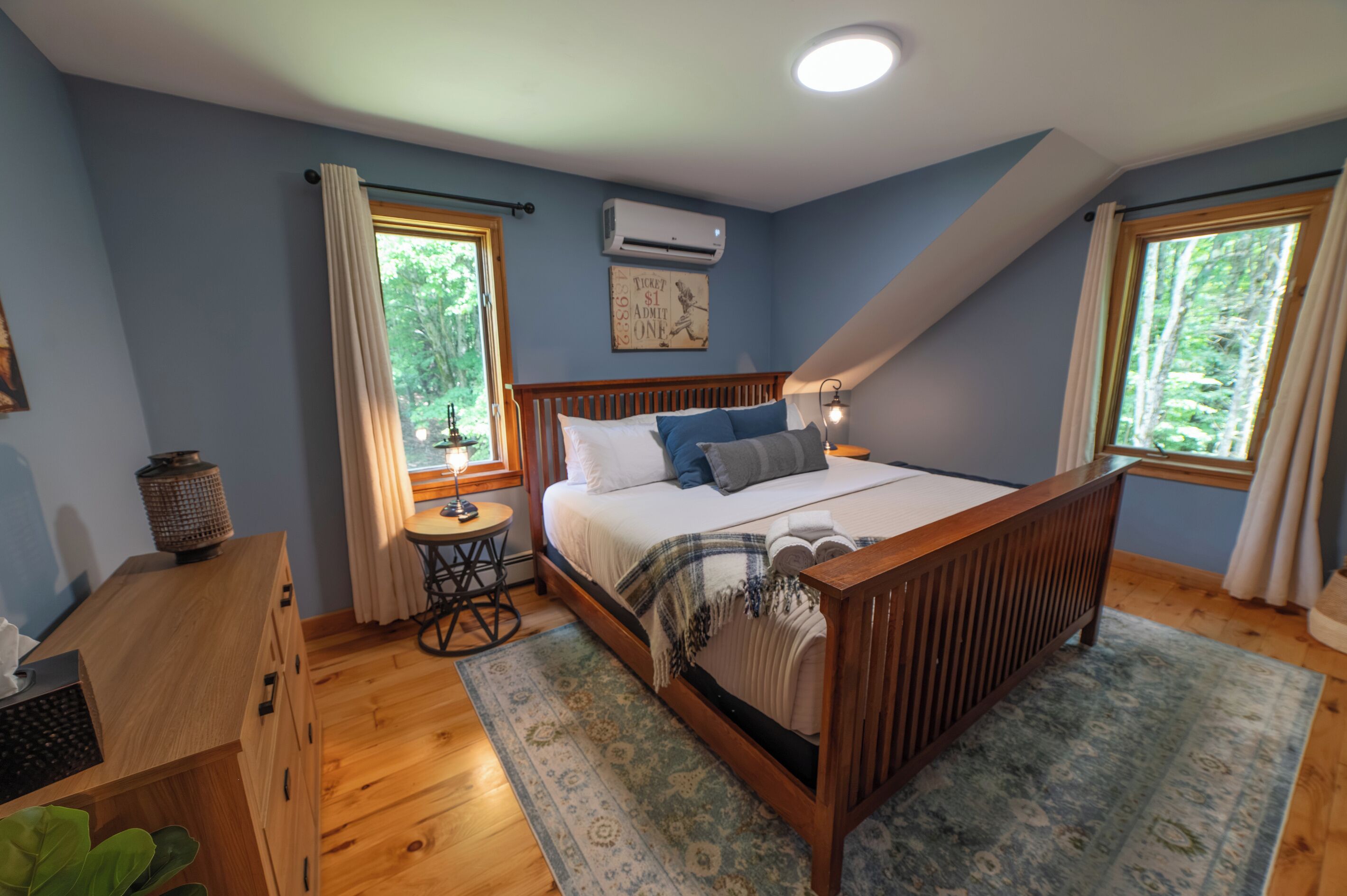 Una camera da letto con un letto di legno, una scrivania, una sedia, un condizionatore d'aria e una finestra con tende.