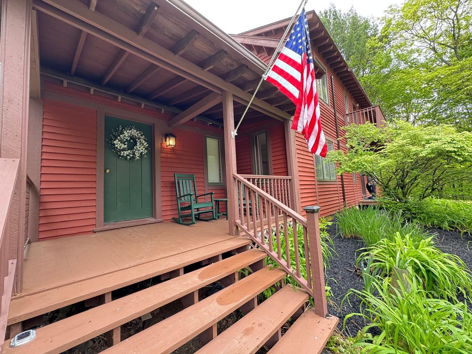 A wooden house with a porch, steps, a green door, and an American flag.