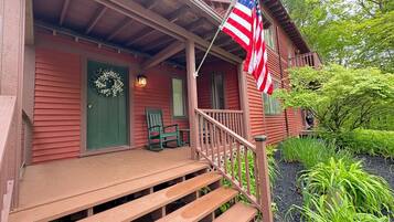 A wooden house with a porch, steps, a green door, and an American flag.