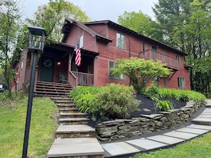 A red wooden house with a porch, stone steps, and a flag. - Newly Renovated; Private Pool Oasis Pics to Come (Cooperstown)