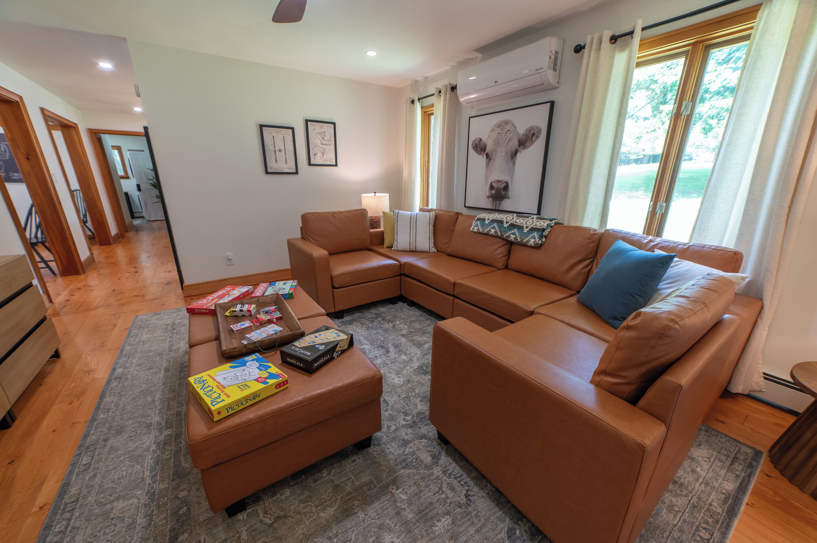Una sala de estar moderna con un sofá seccional, una mesa de centro con juegos de mesa y un ventanal con cortinas.