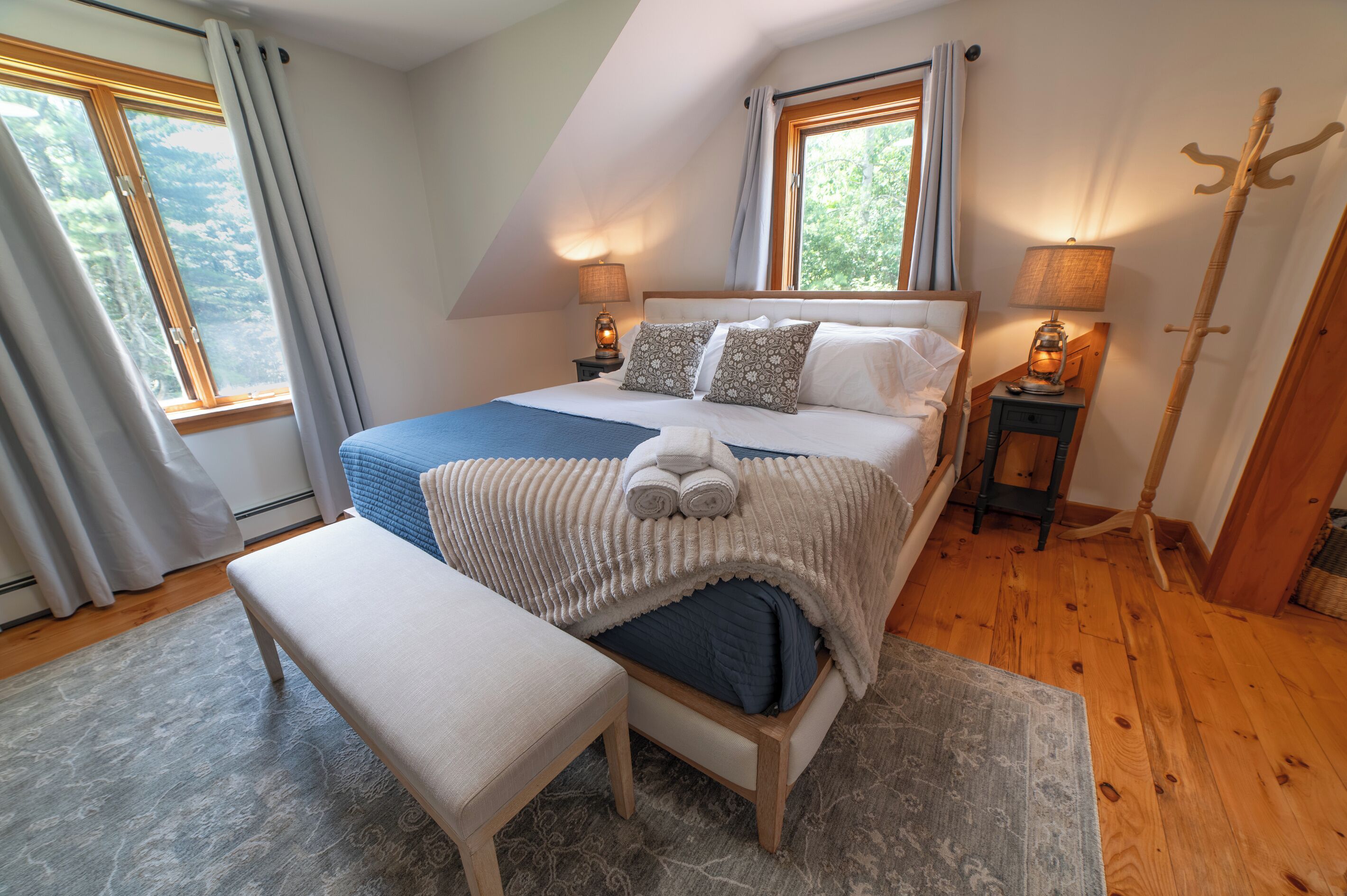 A bedroom with a bed, bench, bedside tables, lamps, and a window with curtains.