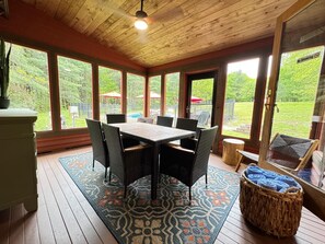 Una habitación con techo de madera, ventanas amplias, una mesa con sillas y vista a un patio trasero.
