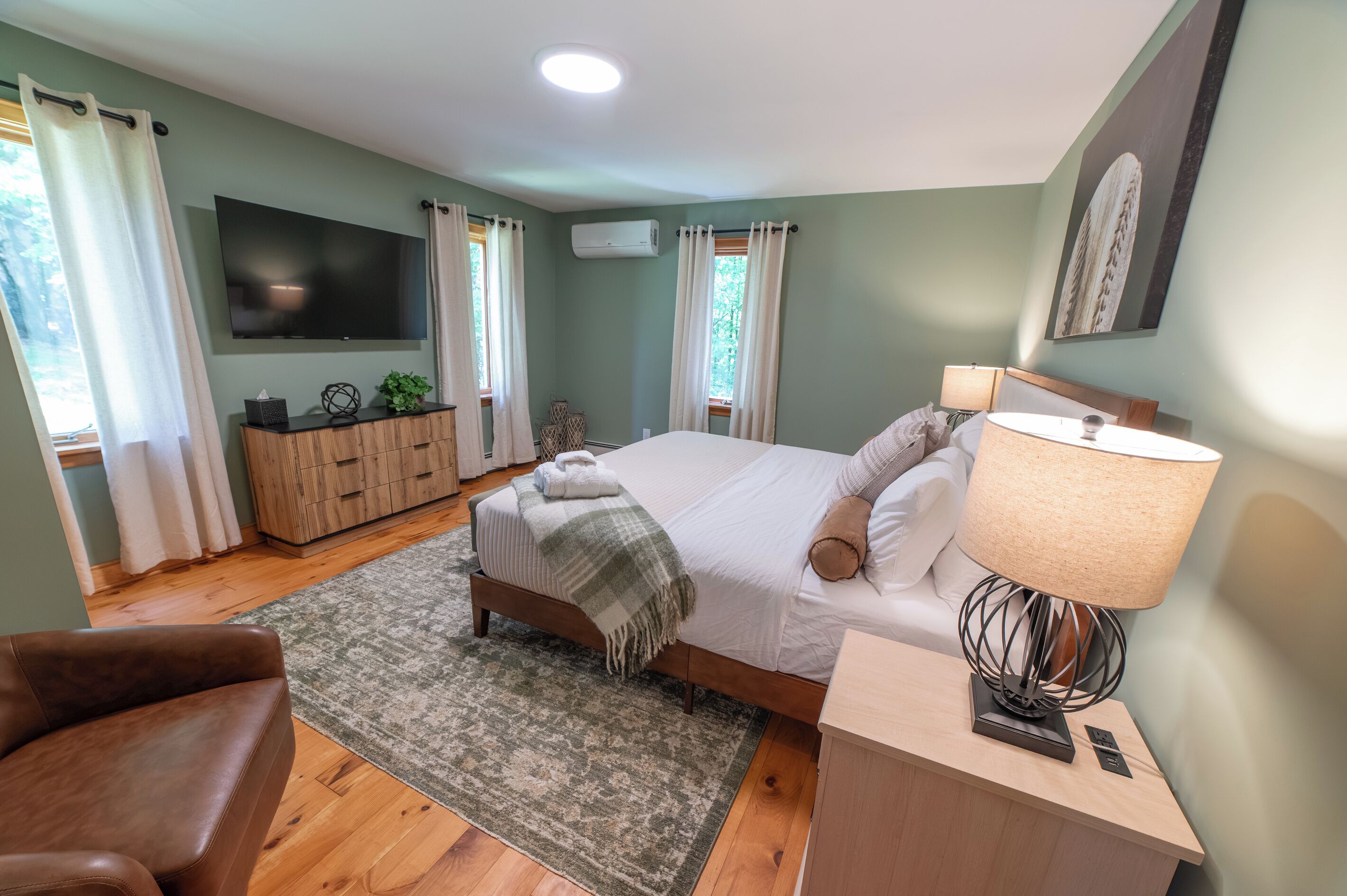 A bedroom with a bed, a TV, a desk, a chair, and a window.