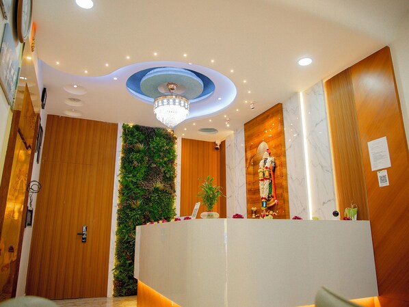A reception area with a wooden reception desk, a green vertical garden, a chandelier, and a marble wall with a statue. - Hotel Venkteshwar (Shorapur)