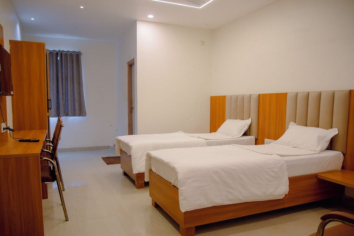 A hotel room with two single beds, a wooden desk, a chair, and a television.