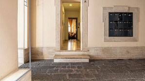 A hallway with a stone floor, a door with a number 'A' above it, and a wall-mounted black object. - Foro Romano Luxury Flat (Rome)