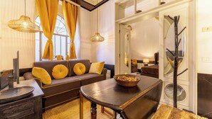 A modern living room with a brown sofa, yellow cushions, a wooden coffee table, and a large window with yellow curtains. - Foro Romano Luxury Flat (Rome)