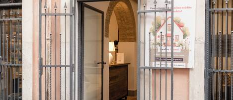 An open metal gate leading to a room with a wooden dresser and a lamp. A poster with a house illustration and text is visible on the wall.