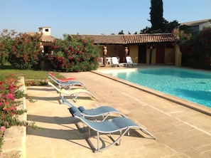 Zona de piscina amb gandules, una piscina i un edifici amb teulada enrajolada.