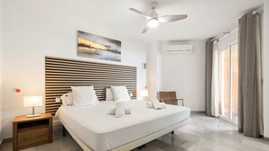 A modern hotel room with a large bed, a ceiling fan, a painting on the wall, and a view of the outdoors through the window. - RDR516 - Sea View Apartment with Pool in Cala de Mijas (La Cala de Mijas)