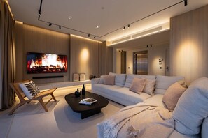 Ein modernes Wohnzimmer mit großem Flachbildfernseher, einer Couch, einem Couchtisch und einem Kamin.