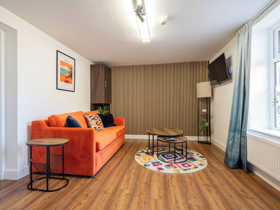 Ein modernes Wohnzimmer mit Holzboden, einer Couch, einem Couchtisch, einem Fernseher und einem Fenster mit Vorhängen.