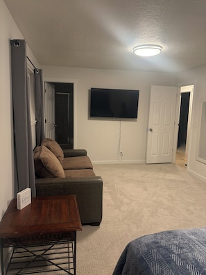 Ein Zimmer mit einem an der Wand befestigten Flachbildfernseher, einem braunen Ledersofa, einem Holztisch und einer bettenausgestalteten Bettdecke.
