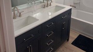 A modern bathroom with two sinks, a large mirror, a shower, and dark cabinetry.
