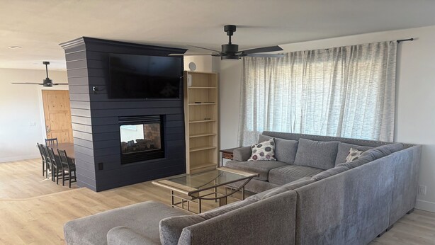 A modern living room with a sectional sofa, a glass coffee table, a fireplace, and a ceiling fan.
