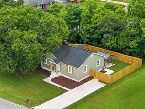 Une maison de plain-pied avec un jardin clôturé, entourée d’arbres.