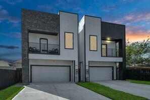 Ein modernes, zweistöckiges Haus mit Garage, Balkon und einer Fassade aus Stein.
