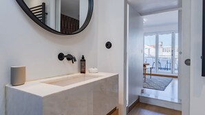 Une salle de bain moderne avec un grand lavabo, un miroir rond et une bouteille de shampoing.